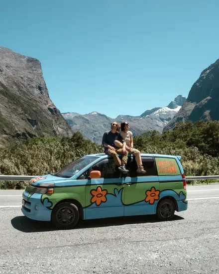 Couple sitting on top of a colourful campervan at a mountain lookout in New Zealand